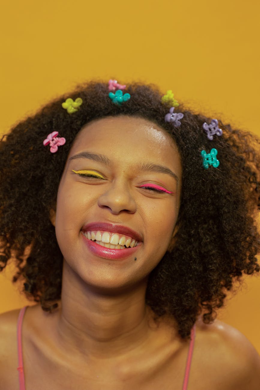 cheerful young black woman with colorful hair clips smiling in yellow studio